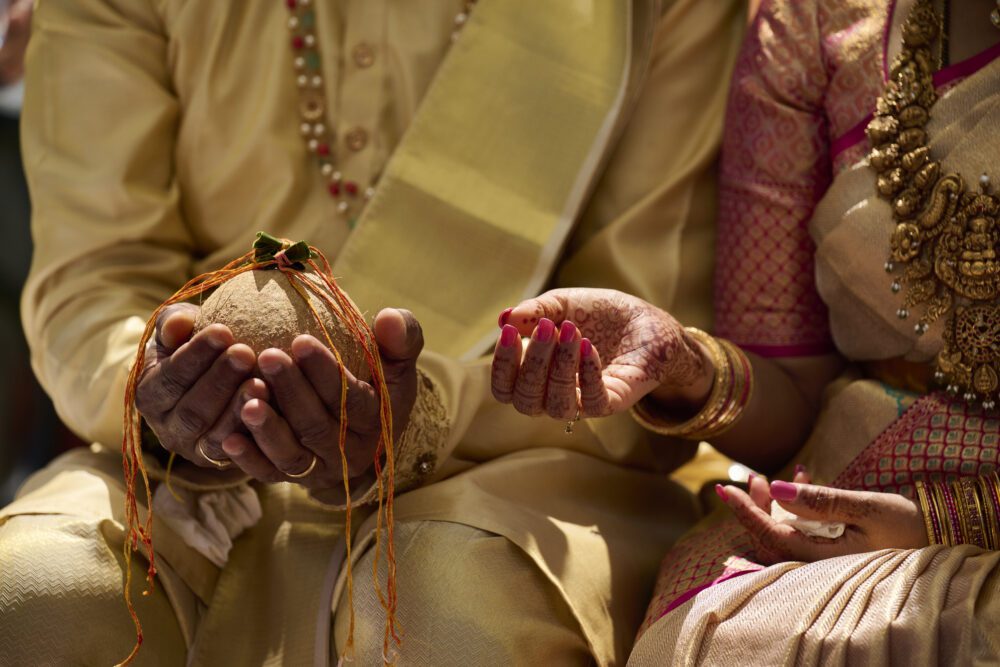 Groom in cream sherwani holding coconut wrapped in red string during wedding ceremony ritual
