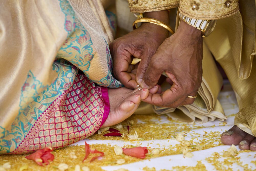 Bride and groom exchange rings during wedding ceremony, hands adorned with gold jewelry and traditional attire